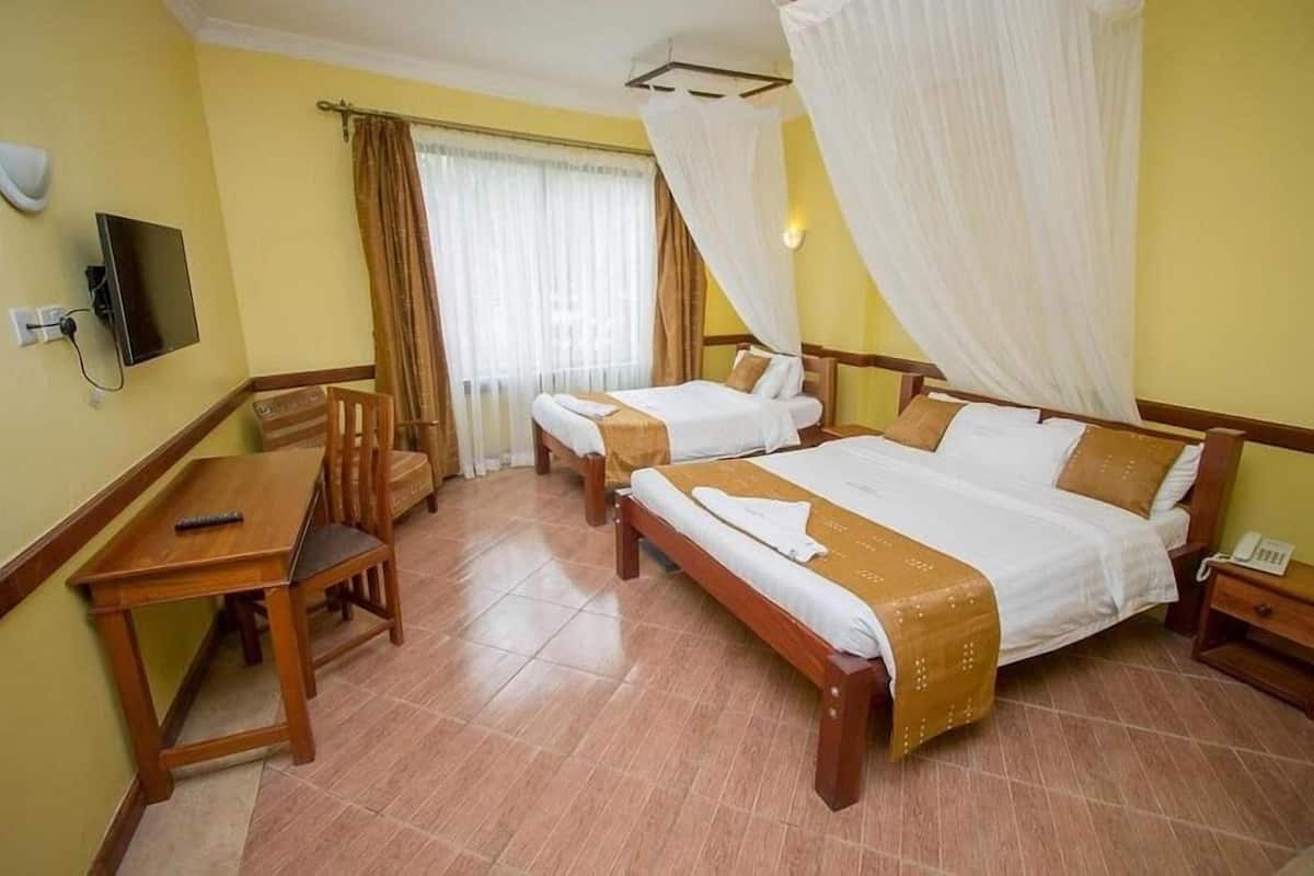 Una habitación de hotel con dos camas individuales, un escritorio de madera, un televisor y una ventana con cortinas.
