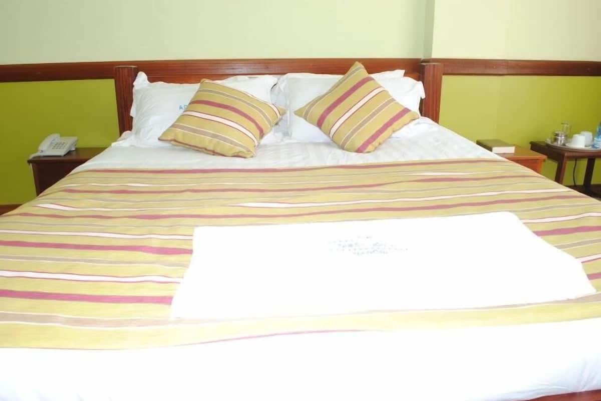 Una cama con ropa de cama a rayas, dos almohadas, un teléfono en la mesita de noche y una pequeña mesa con una taza y un platillo.