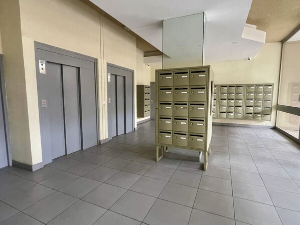 A hallway with grey doors, a metal mail rack, and a tiled floor.