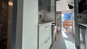 A modern kitchen with white cabinets, a stainless steel refrigerator, and a view of a dining area with a table and chairs. - Studio for 4, near chairlift, WiFi, parking - SuperDévoluy (Le Dévoluy)