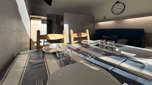 A dining area with a table set for two, a television mounted on the wall, and a clock above the table. - Studio for 4, near chairlift, WiFi, parking - SuperDévoluy (Le Dévoluy)