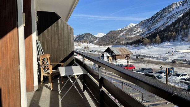 A balcony with a view of a snowy mountain landscape, a parking area, and a small building in the distance.