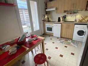 Cozinha compacta com área de refeições, incluindo uma mesa com xícaras e uma cadeira, uma máquina de lavar e uma pia.