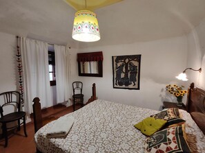 Une chambre à coucher avec un lit, des chaises, une lampe suspendue, une décoration murale et une fenêtre avec des rideaux.