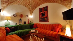 Una sala de estar acogedora con un sofá verde y naranja a rayas, una mesa de centro de madera y un televisor montado en la pared.