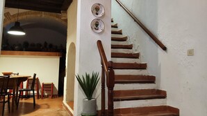 Una escalera de madera con barandilla, que lleva a un rellano con una planta en maceta y dos platos decorativos.