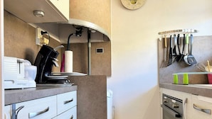 A modern kitchen with a built-in oven, a coffee machine, and a set of kitchen utensils hanging on the wall.