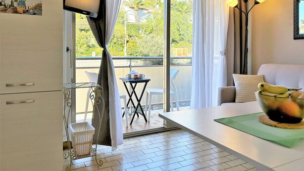 A modern hotel room with a balcony, a dining table, a TV, and a bowl of fruit.