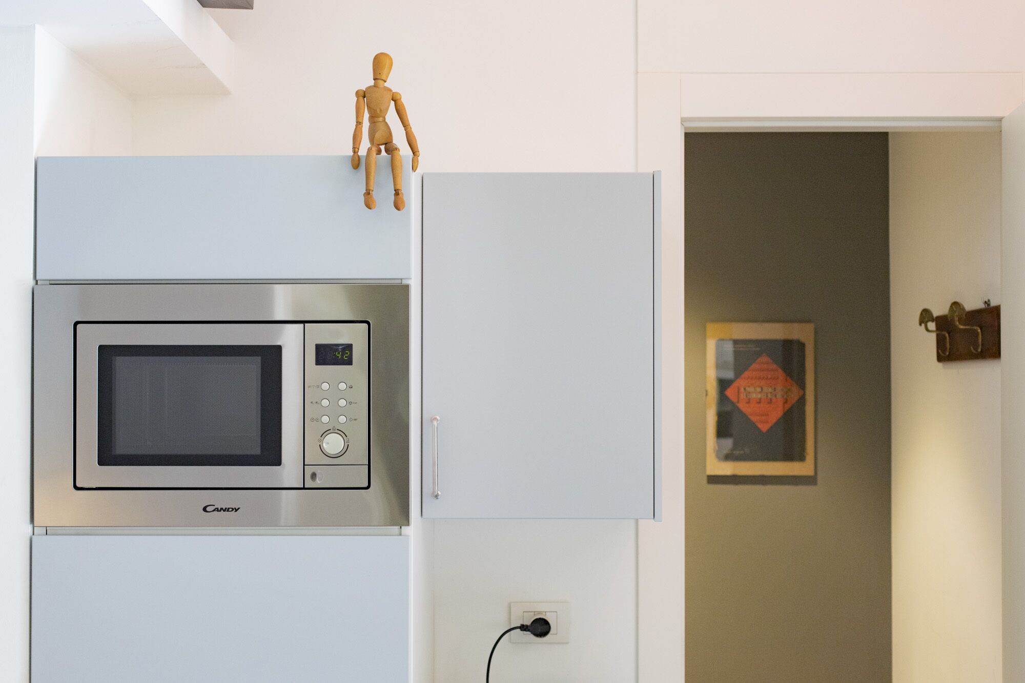 Una cocina con microondas integrado, una figura de madera encima del gabinete y un cartel enmarcado en la pared.
