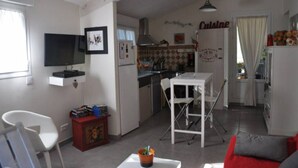Een kleine woonruimte met een keuken, een eethoek en een aan de muur bevestigde televisie.