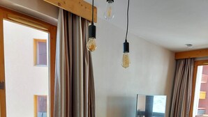 Habitación de hotel con una mesa de comedor de madera, sillas, un televisor en una cómoda y una ventana con cortinas.