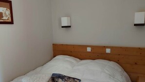 Una cama bien hecha con una colcha blanca y un cojín con un diseño de lobo. Hay dos lámparas de pared y un cuadro en la pared.