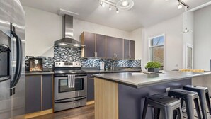 Eine moderne Küche mit dunklen Schränken, Edelstahlgeräten, einer großen Kochinsel mit Barhocker und einer dekorativen Spritzschutzwand.