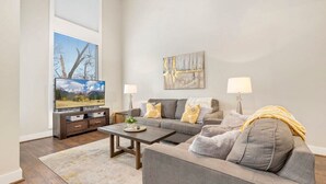 Ein Wohnzimmer mit grauem Sofa, einem Couchtisch, einem Fernseher und einem Bild an der Wand.