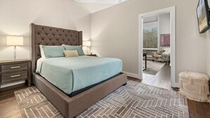 Ein Schlafzimmer mit einem großen Bett, einem Nachttisch, einem an der Wand befestigten Fernseher und einer Tür, die auf einen Balkon führt.
