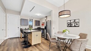 A modern kitchen with a central island, dining table with chairs, and a hanging light fixture. - Frisco Suite - 0.1 mi to MTB trail Walk to DT Fay (Fayetteville)