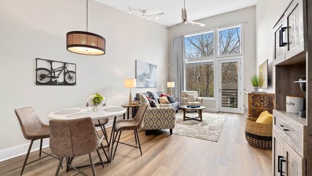 A modern living room with a round dining table, comfortable seating, and a large window offering a view of the outdoors. - Frisco Suite - 0.1 mi to MTB trail Walk to DT Fay (Fayetteville)