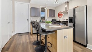 A modern kitchen with a central island, stainless steel appliances, and a 'Welcome' sign on the wall. - Frisco Suite - 0.1 mi to MTB trail Walk to DT Fay (Fayetteville)