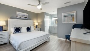 A bedroom with a bed, bedside tables, a ceiling fan, a bathroom with a mirror, and a desk.