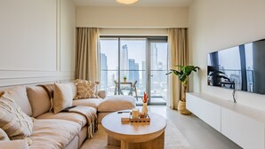 A modern living room with a sofa, a coffee table, a TV, and a view of a cityscape through large windows. - Exquisite 2BR - Breathtaking BurjSkyline (Dubai)