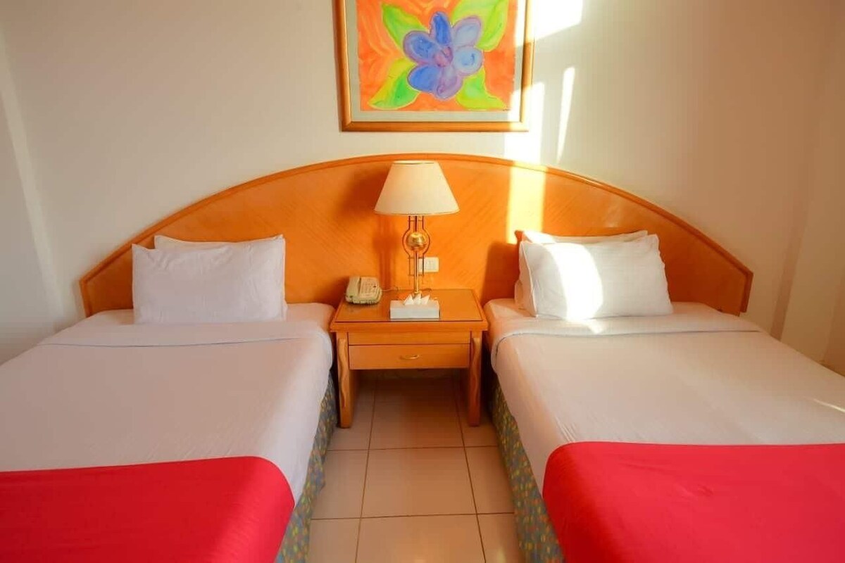 Una habitación de hotel con dos camas, una mesita de noche con una lámpara y un cuadro en la pared.