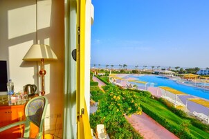 A balcony with a view of a swimming pool, a chair, a table with a lamp, and a window.