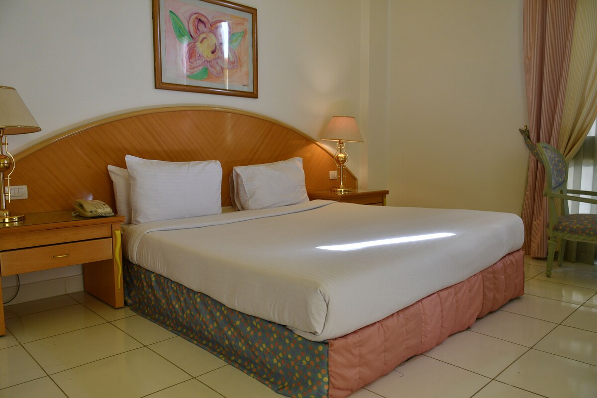 Habitación de hotel con una cama grande, dos mesitas de noche, una silla y un cuadro en la pared.
