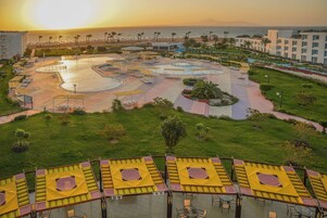 A resort with a pool area, sun loungers, and a view of the sea at sunset.