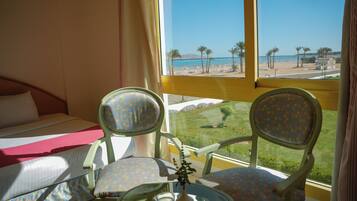 A hotel room with a bed, two chairs, a small table, and a view of the beach.
