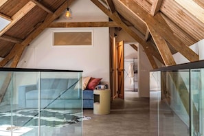 A loft-style room with exposed wooden beams, a glass table with a cowhide rug, a blue sofa, and a small round table with a cup. - Hoeve de Lente | Historic Farmstead Near Breskens (Breskens)