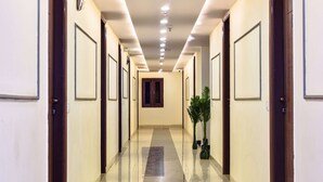 A long, well-lit hallway with doors on both sides, a central window, and a potted plant on the right. - HOTEL YASH PALACE (New Delhi)