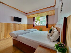 A double bed with a wooden headboard, a flat-screen TV mounted on the wall, and a window with curtains. - Cozy Homestay (Darjeeling)