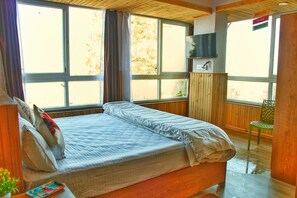A bedroom with a bed, a TV, and large windows. - Cozy Homestay (Darjeeling)