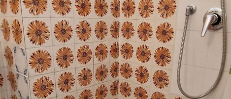 Une salle de bain comprenant des toilettes, un bidet et une douche. Les murs sont recouverts de carreaux décorés d’un motif floral.