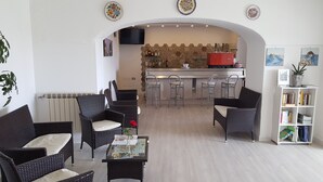 A cozy living room with wicker furniture, a coffee table with magazines, and a bookshelf. - Hotel Bellavista (Forio)