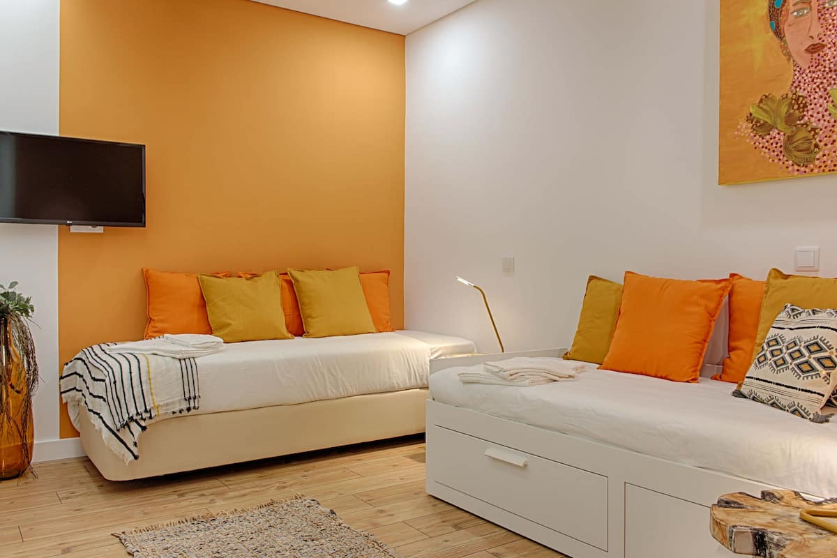 A modern bedroom with two beds, a flat-screen TV, and a large painting.