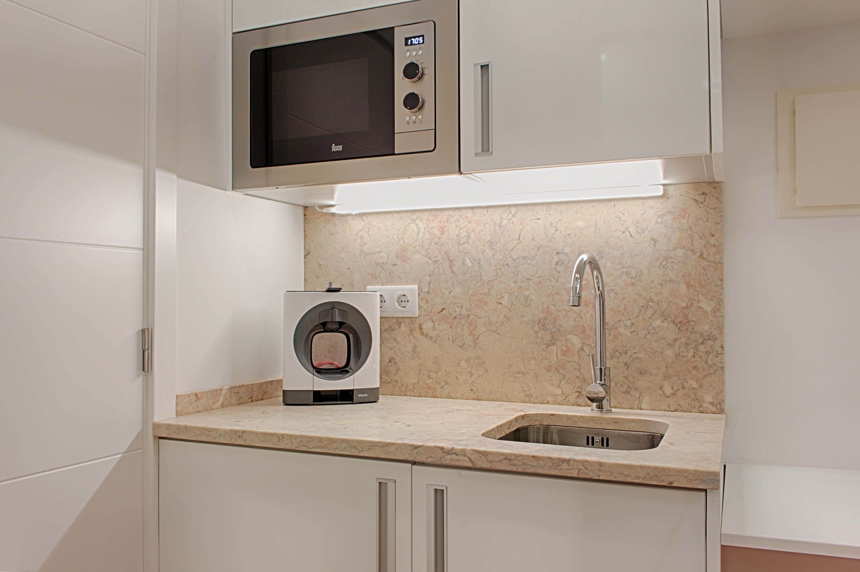 Una cocina compacta con microondas integrado, cafetera y pileta de acero inoxidable.