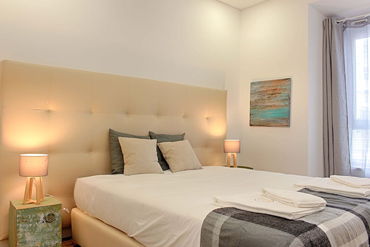 A neatly made bed with a white duvet, two bedside lamps, and a small bedside table with a lamp.