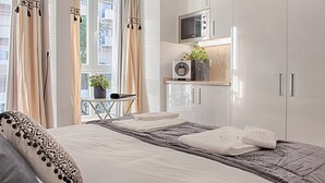 A modern hotel room with a neatly made bed, a small table with a plant, a microwave, and a window with curtains. - GuestHouse by Trip2Portugal (Lisbon)