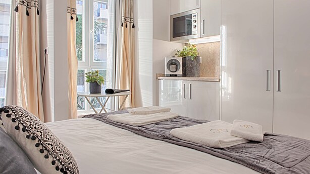 A modern hotel room with a neatly made bed, a small table with a plant, a microwave, and a window with curtains. - GuestHouse by Trip2Portugal (Lisbon)