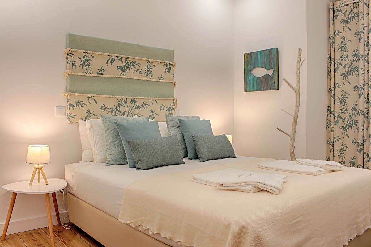 A neatly made bed with a white and green headboard, multiple pillows, and a bedside lamp.