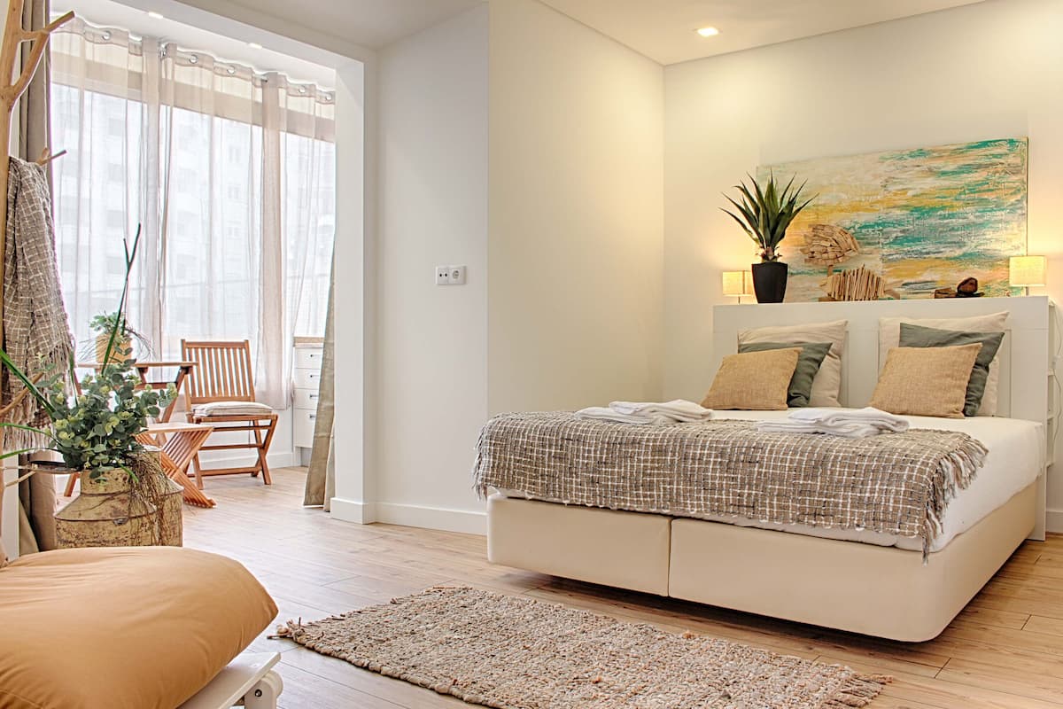 A modern bedroom with a large bed, a wooden chair, a small table, and a potted plant.
