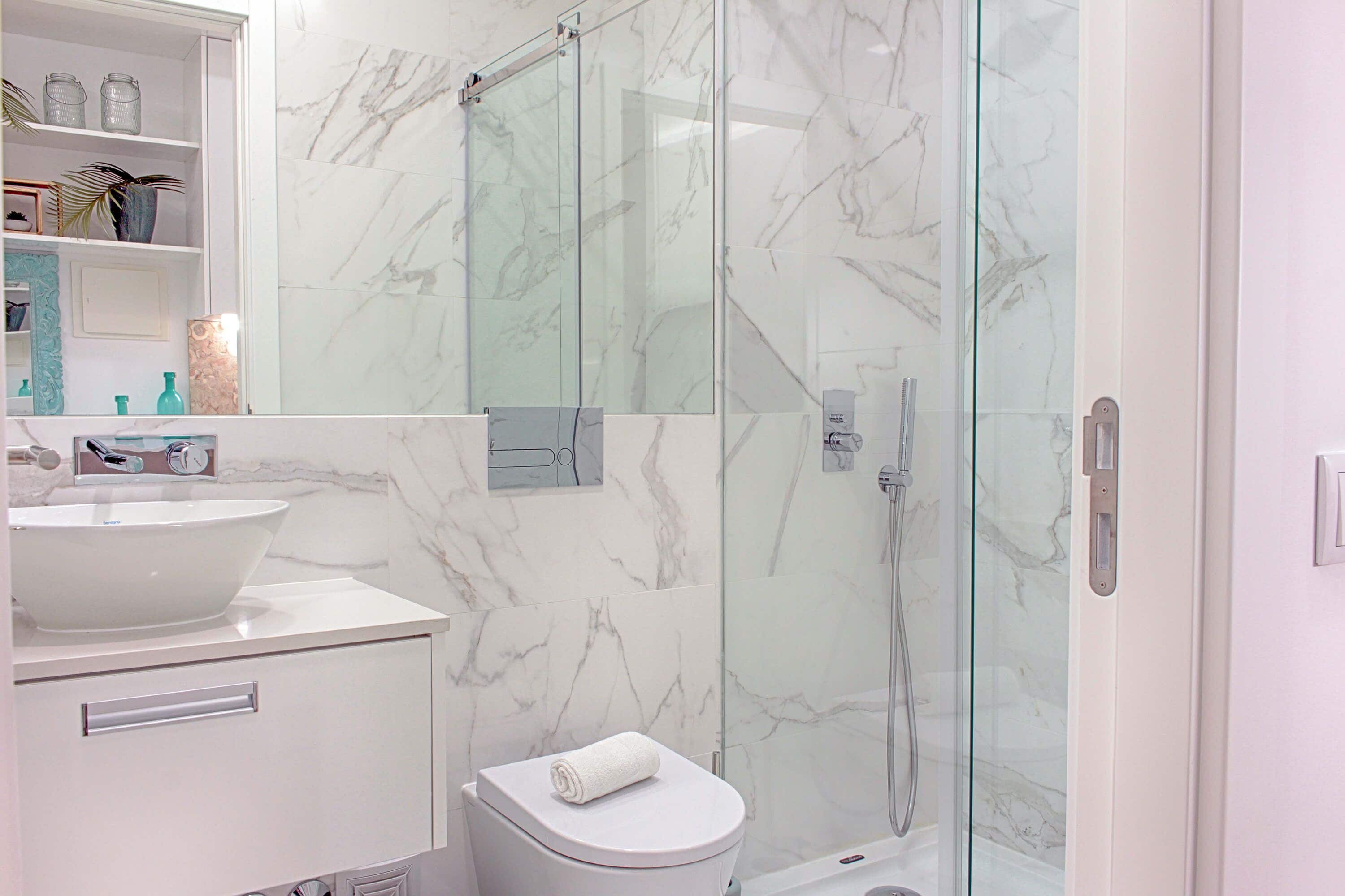 A modern bathroom with a marble sink, toilet, and glass-enclosed shower.