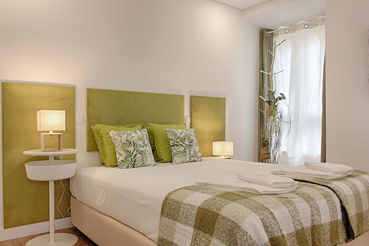 A neatly made bed with green and white pillows, two bedside lamps, and a checkered throw blanket.