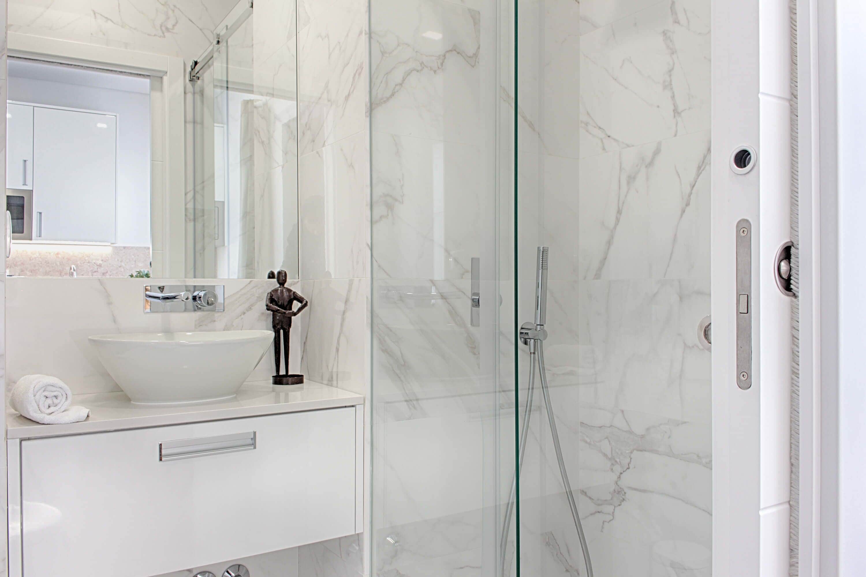 Un bagno moderno con un ampio lavandino bianco, cabina doccia in vetro e schienale in marmo.