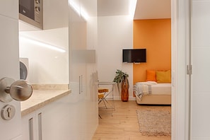A modern apartment with a kitchen, dining area, and a bedroom with an orange accent wall and a TV mounted above the bed. - GuestHouse by Trip2Portugal (Lisbon)