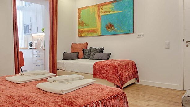 A bedroom with two beds, a large abstract painting, and a view of the kitchen. - GuestHouse by Trip2Portugal (Lisbon)