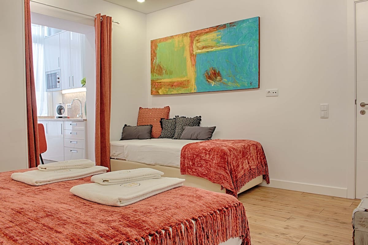 A bedroom with two beds, a large abstract painting, and a view of the kitchen.