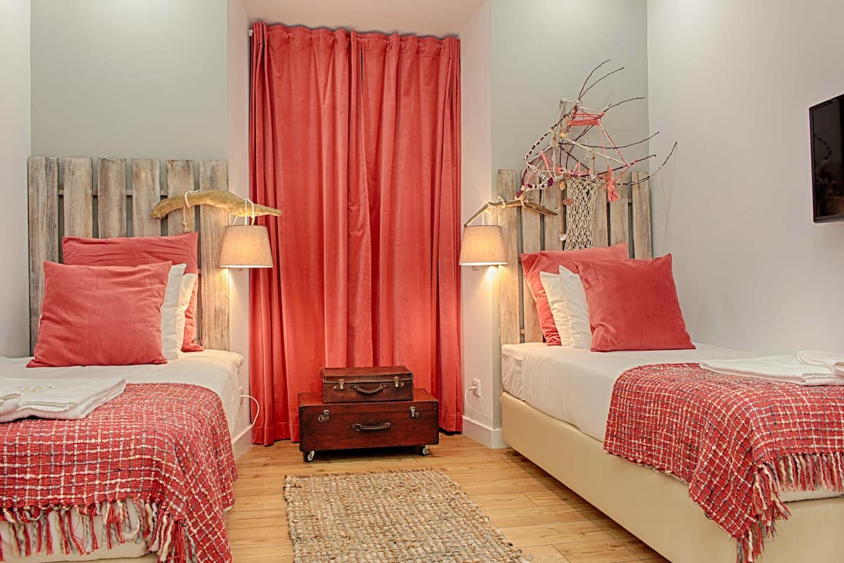 A bedroom with two beds, red curtains, wooden headboard, and a decorative wall piece.