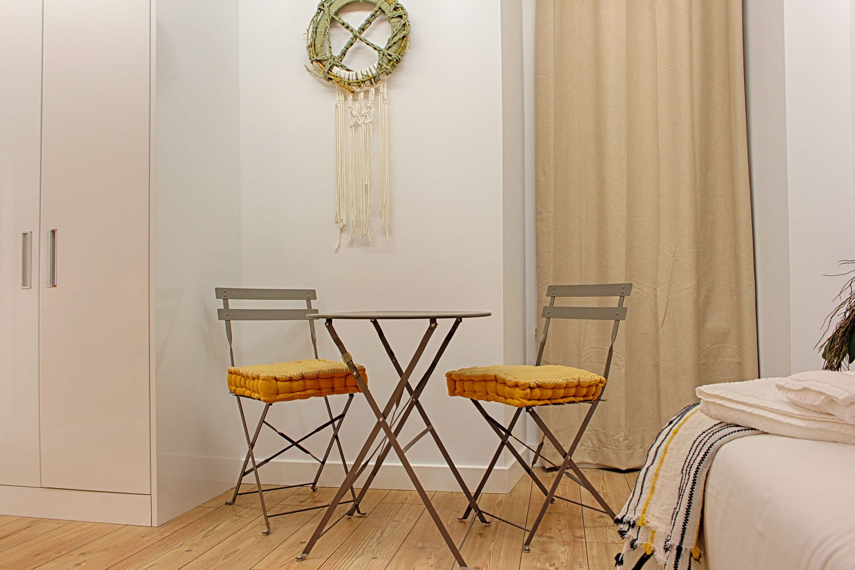 A room with a bed, a small table with two chairs, a wardrobe, and a wall decoration.
